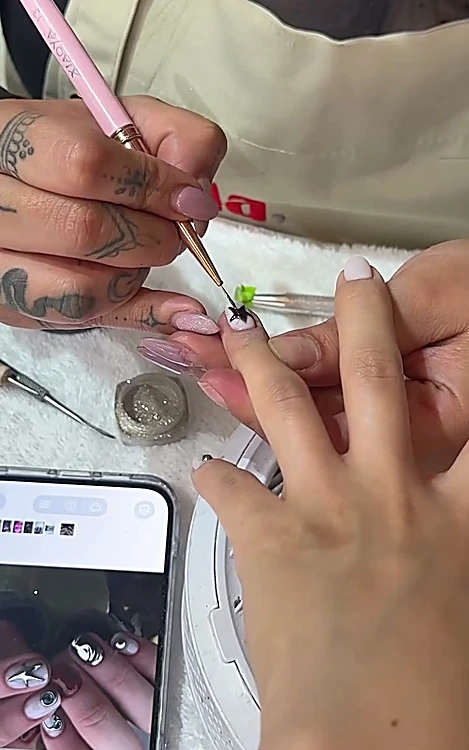 Manicurista pintando un diseño mientras ve la foto de referencia en un celular