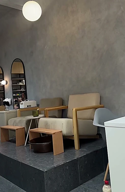 Interior de hula: sillones arena, tinas de cobre para pedicure, espejos en arco y lámpara de globo sobre muro de microcemento