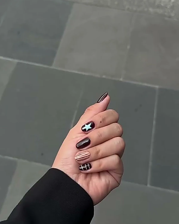 Uñas color vino con estrella blanca y líneas, sobre piso de piedra gris